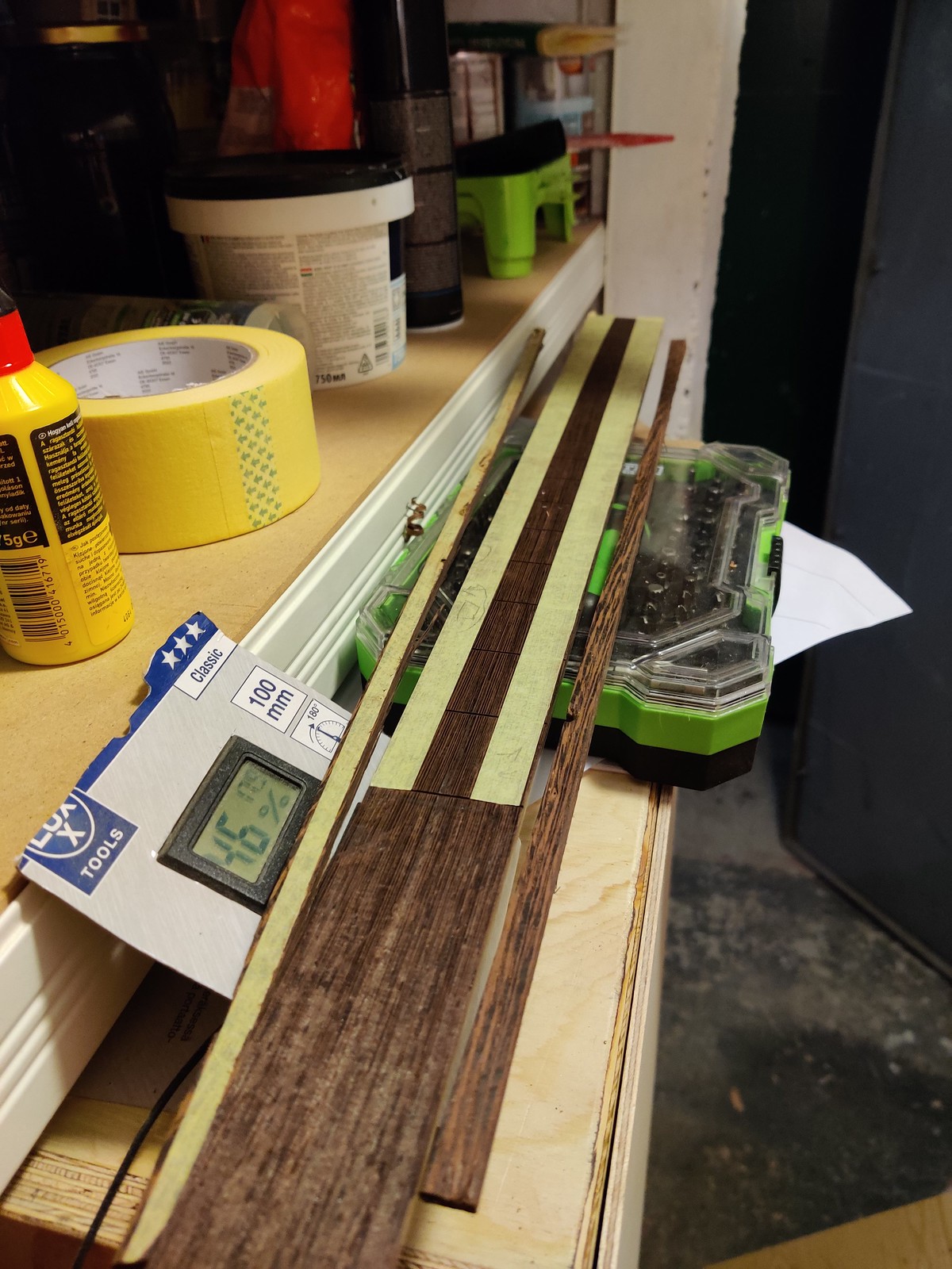 A wenge fretboard blank with two binding pieces next to a higrometer